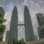 Low-angle view of Petronas Twin Towers in Kuala Lumpur with a cloudy sky backdrop.