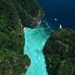 A stunning aerial view of a turquoise lagoon in Thailand filled with boats and surrounded by lush cliffs.